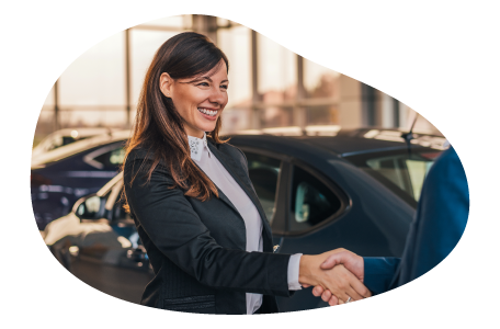 An employee shakes hands with a customer in a car dealership's showroom. An employee shakes hands with a customer in a car dealership's showroom.