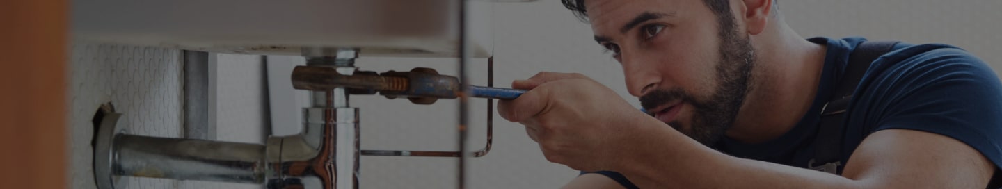 A plumber tightens a pipe with a wrench.