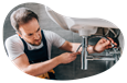 A plumber attaches a water line underneath a sink.