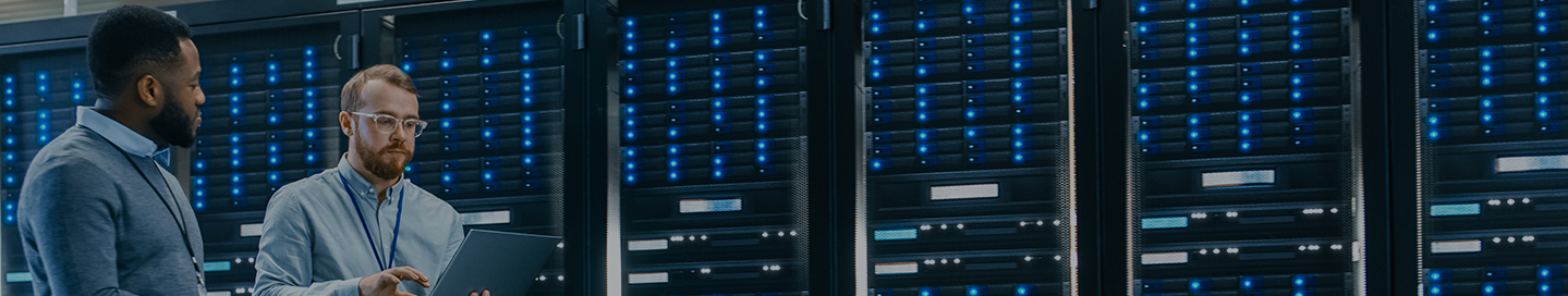 Two technicians working on a laptop inside a cloud computing server room.