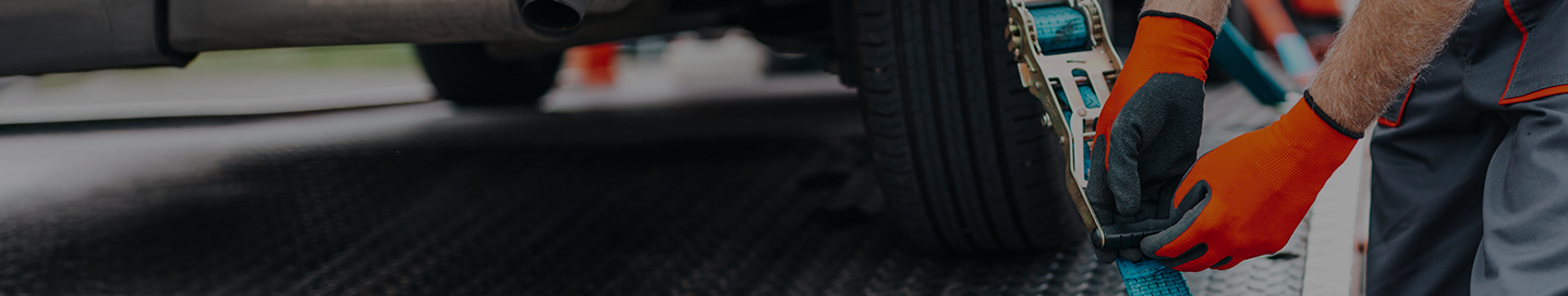 A towing company employee secures the tie-down straps on a flatbed truck.
