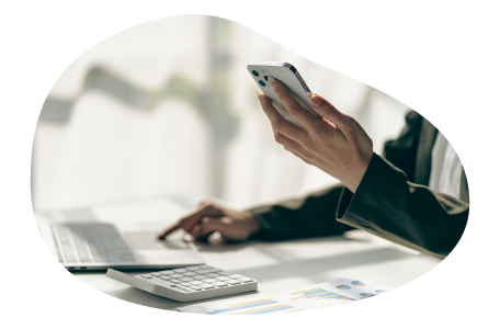 A small business owner using smartphone and laptop with calculator and charts on desk. A small business owner using smartphone and laptop with calculator and charts on desk.